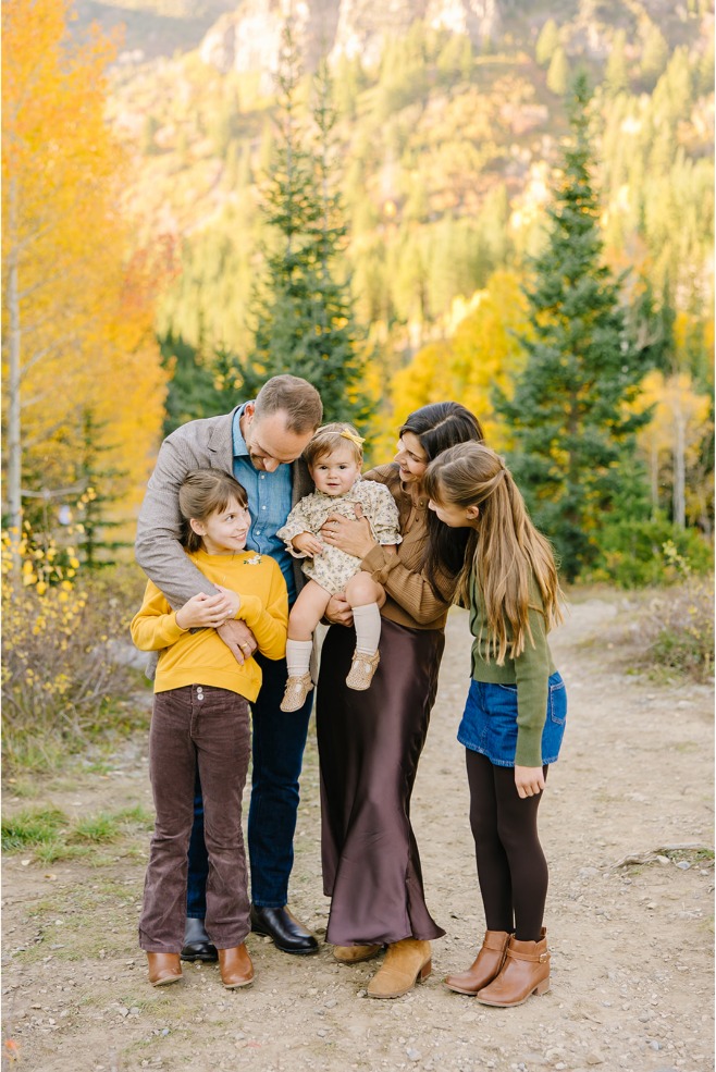 Family of five laughing together in a huddle on a canyon trail with golden aspens behind