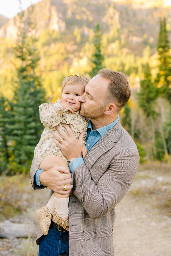 Dad kissing his baby girl's cheek with blurred mountains behind