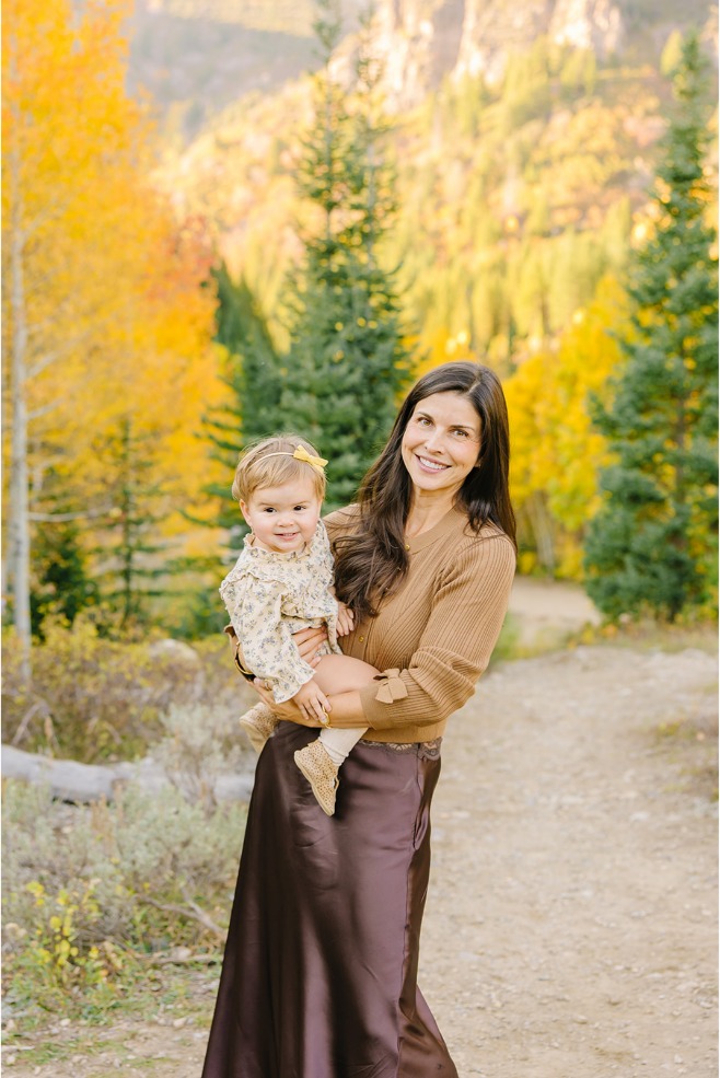Mom smiling while holding her baby girl in front of golden aspens