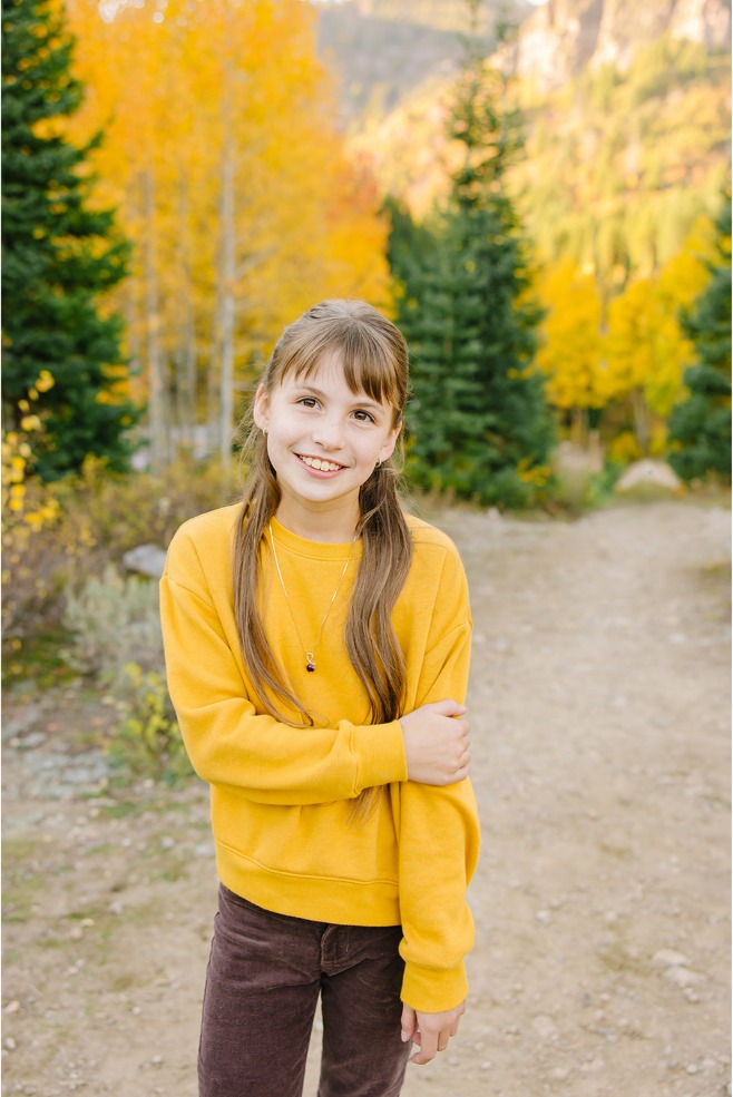 Close-up of a smiling girl in a mustard yellow sweatshirt on a fall canyon trail