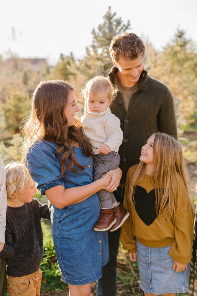 Mom holding toddler with dad and sister at a Utah Christmas tree farm
