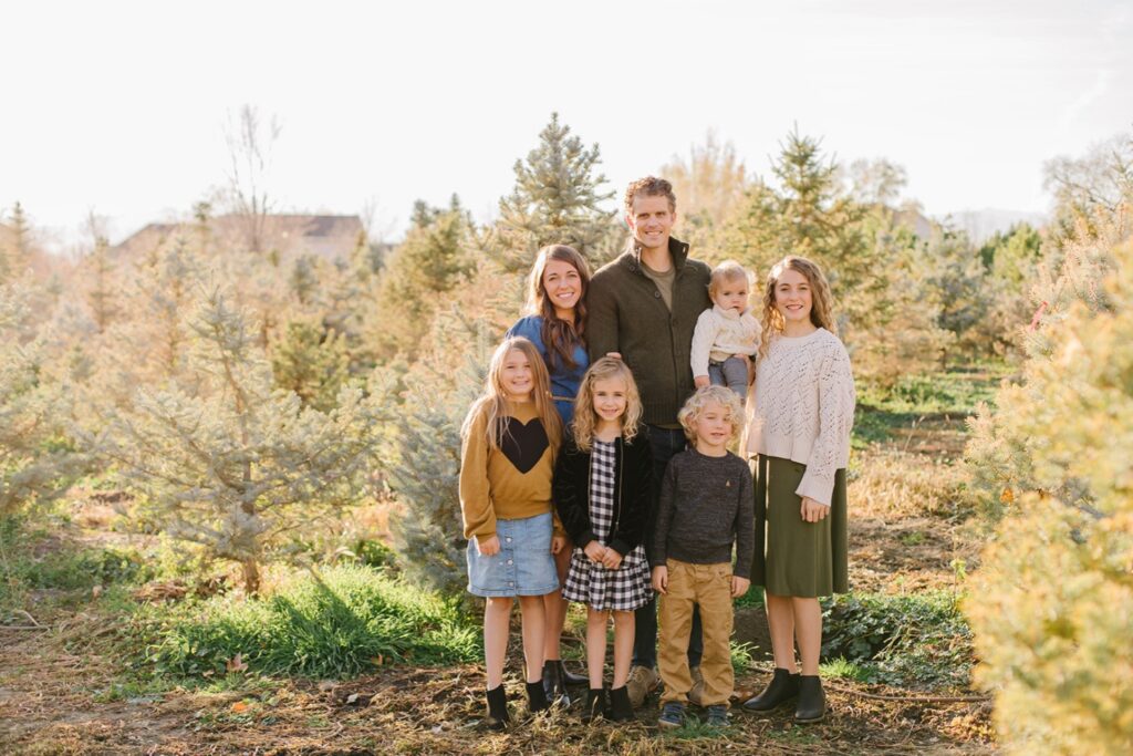 Family of seven standing among blue spruce rows at a Utah Christmas tree farm