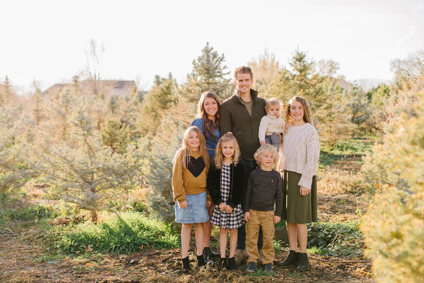 Family of seven standing among blue spruce rows at a Utah Christmas tree farm