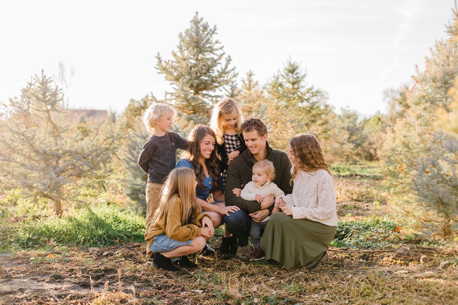 Family kneeling together during golden hour at a Christmas tree farm