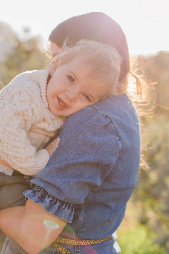 Toddler snuggling into mom, backlit at a Christmas tree farm
