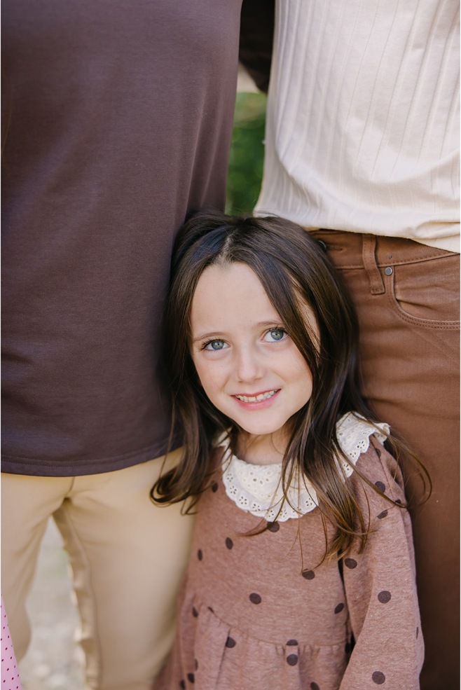 Little girl peeking out between her mom and dad in a close-up family portrait