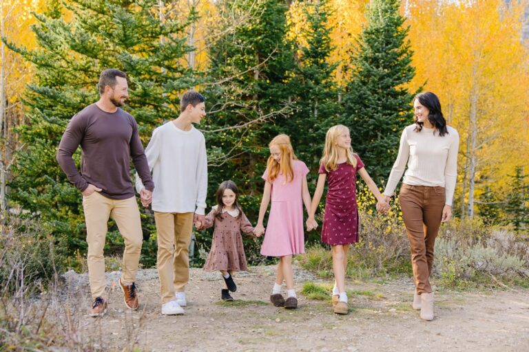 Family of six walking hand in hand down a dirt canyon trail lined with golden aspens
