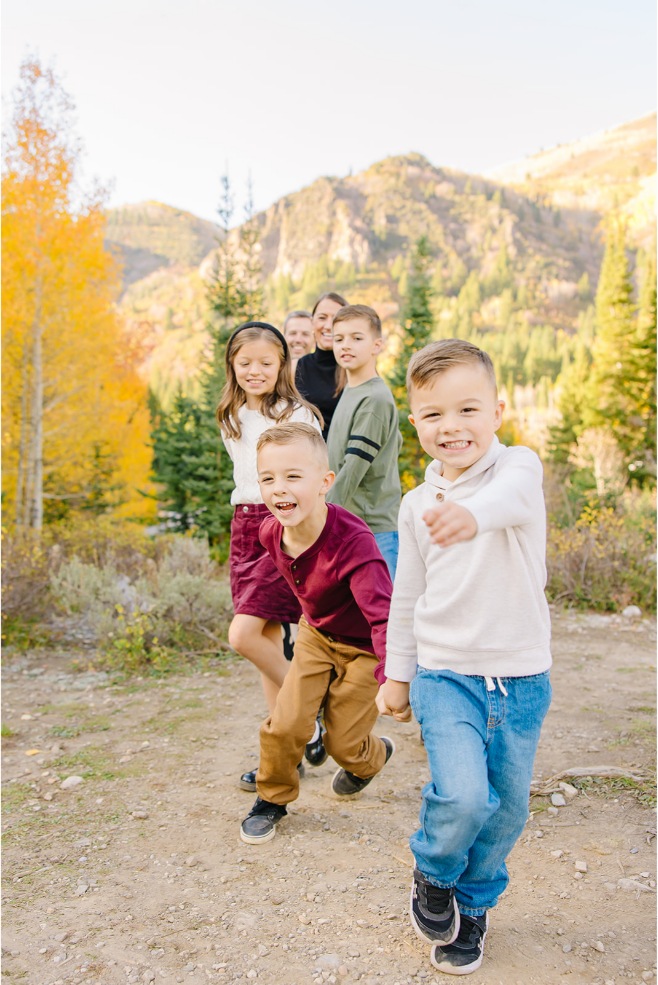 Kids running toward the camera on a dirt trail with parents behind and mountains in the background