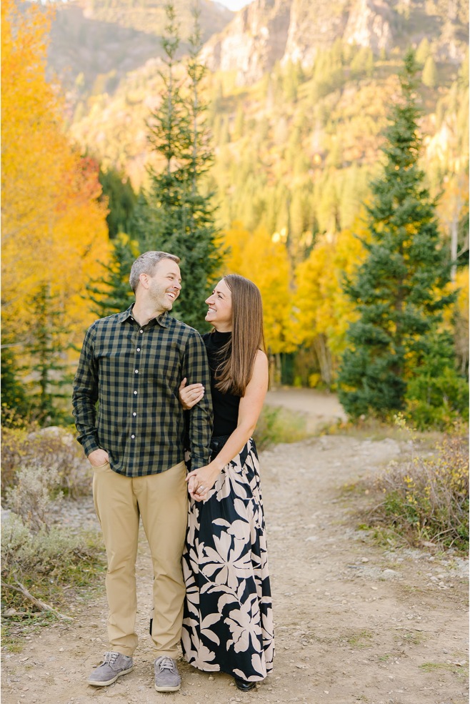 Husband and wife arm in arm laughing at each other during fall family photos in the Utah aspens