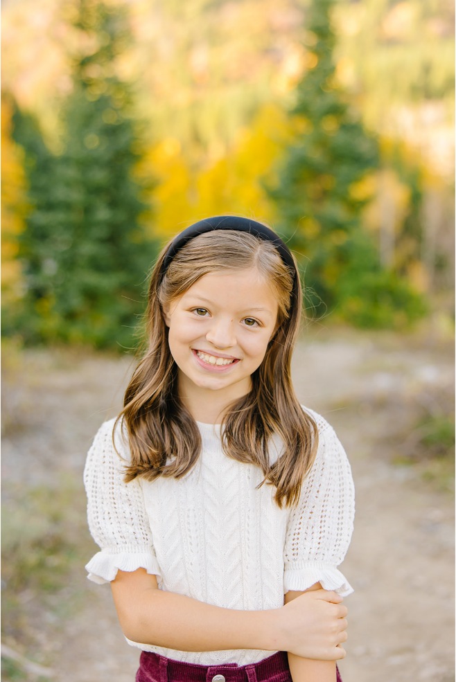 Close-up of a girl in a cream knit sweater and headband in front of golden fall leaves
