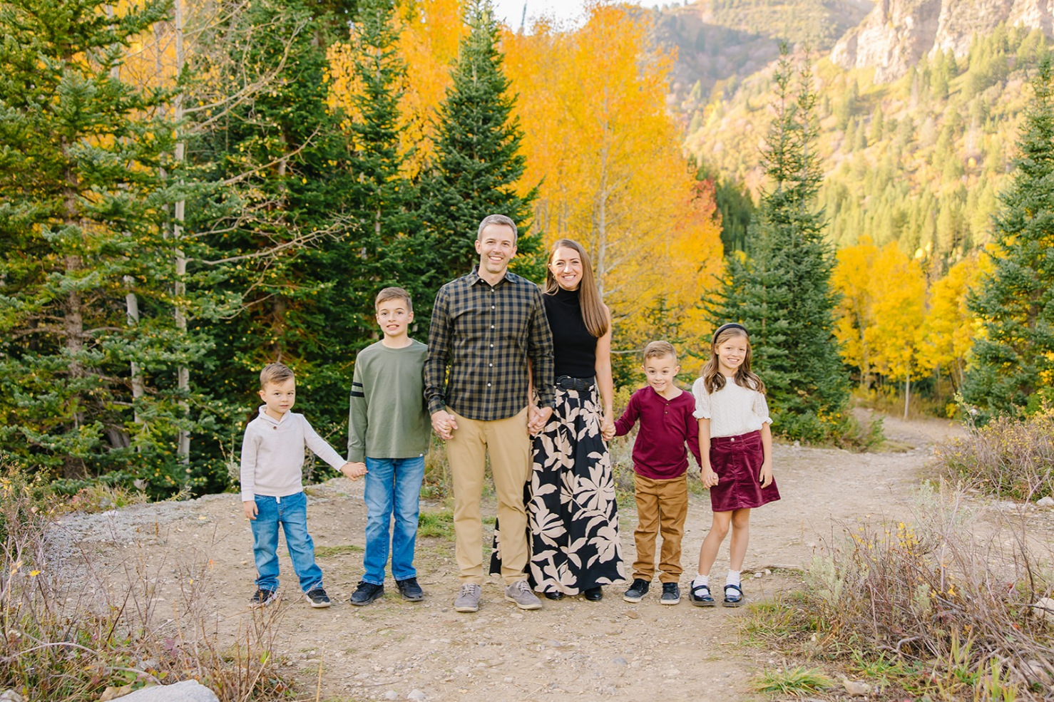 Family of six holding hands in a line among peak golden aspens on a Utah canyon trail