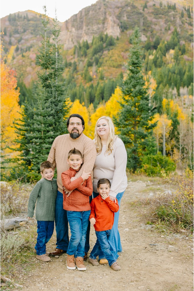 Family of five posed on a dirt trail with bright yellow aspens and a rocky mountain behind