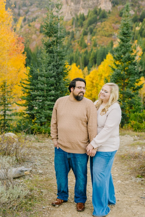 Husband and wife holding hands and looking at each other in front of fall aspens