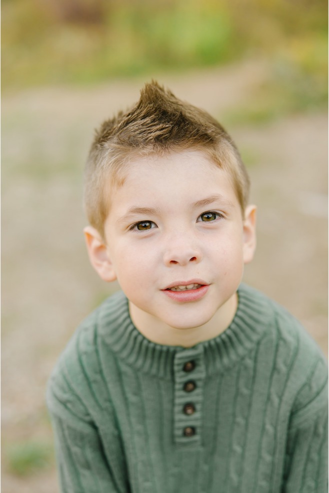 Close-up portrait of a boy in a sage green cable-knit sweater with fall color behind him