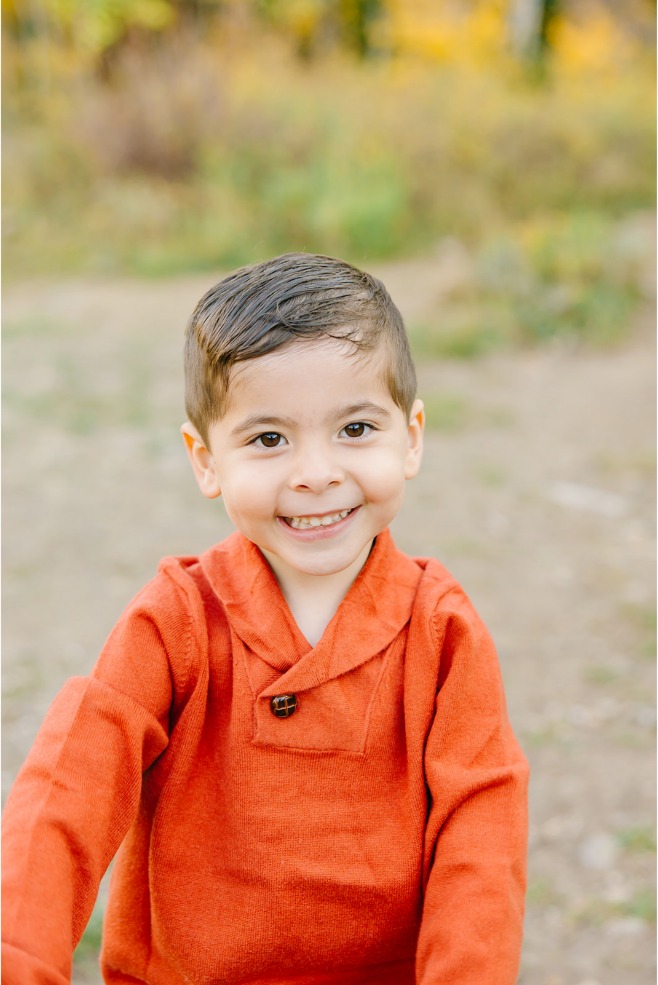 Close-up portrait of a smiling little boy in a rust orange shawl-collar sweater
