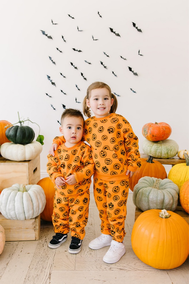 Siblings in matching jack-o'-lantern sweatsuits smiling during a Utah Halloween mini session