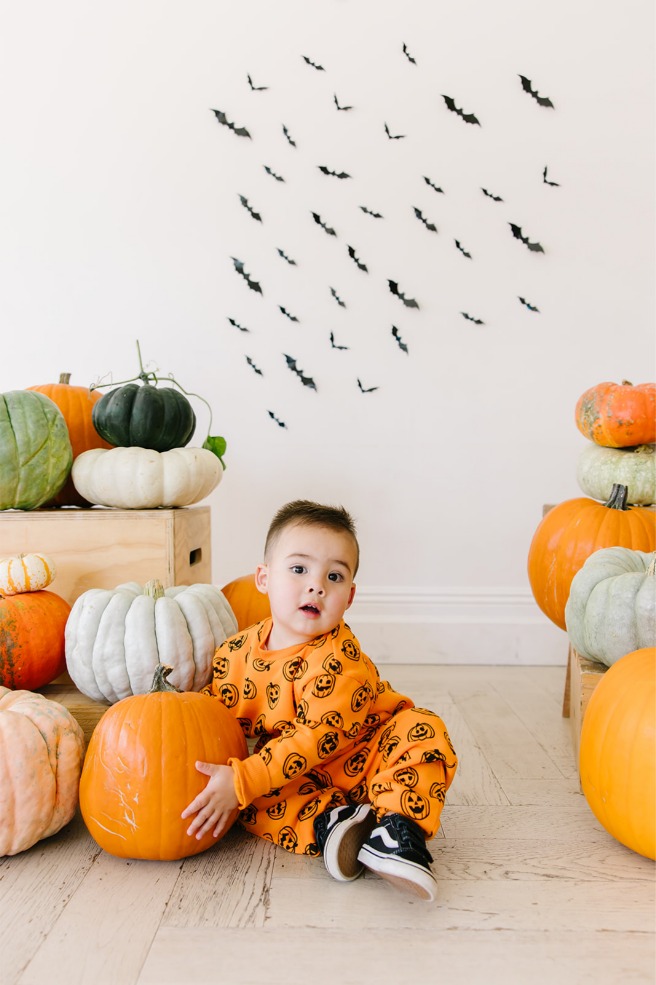 Toddler boy seated with a pumpkin in a jack-o'-lantern sweatsuit at a Utah Halloween mini