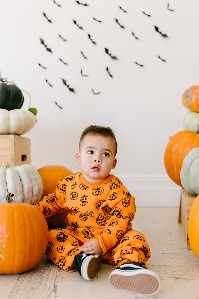 Toddler boy looking up beside stacked orange and white pumpkins in a bright Utah studio